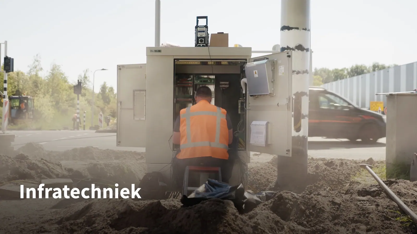 Monteur aan een verkeersregelkast langs de weg, met de tekst “Infratechniek”